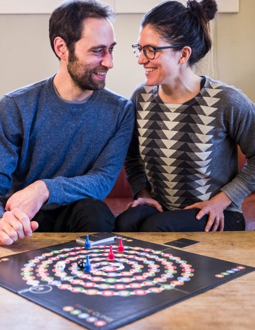 Finkel and Cook smile at each other sitting behind the game they developed together